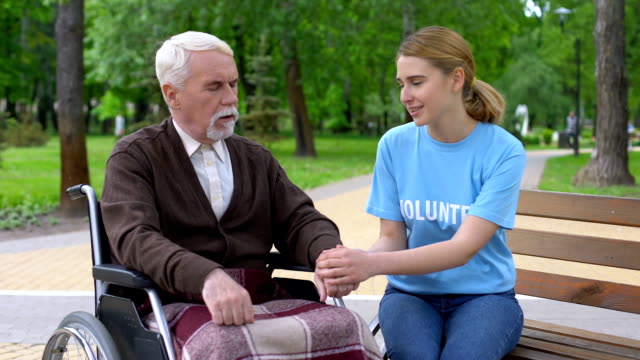 Bonita-mujer-voluntaria-apoyando-pacientes-varones-ancianos-en-silla-de-ruedas,-asistencia