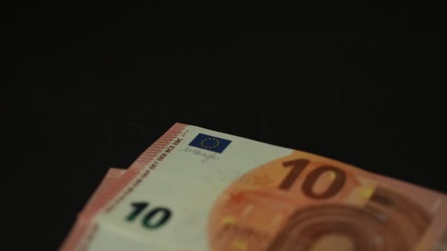Billetes-10-euros-cayendo-lentamente-sobre-la-mesa-negra.-Closeup.-Cámara-lenta