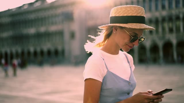 Beautiful-caucasian-woman-in-trendy-outfit-walking-on-square-in-old-city-reading-income-message-on-smartphone-connected-to-4G-internet