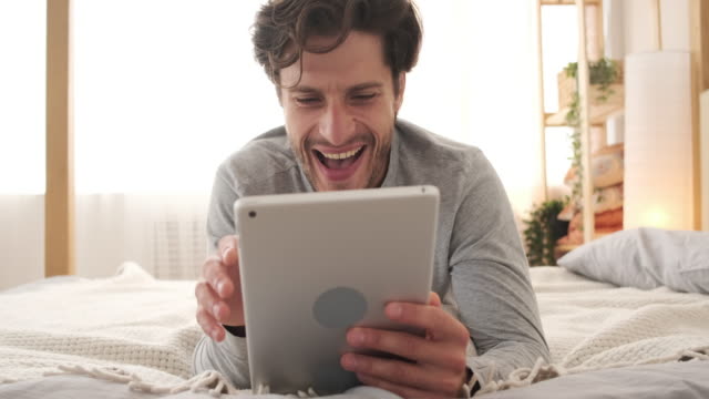 Hombre-alegre-usando-tableta-digital-en-la-cama