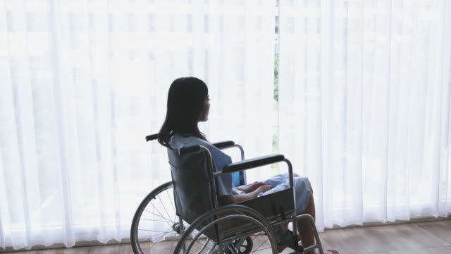 Asiatische-Frauen-Patient,-behinderte-Bein-sitzen-im-Rollstuhl-und-hat-Depressionen-in-einem-Haus-oder-Krankenhaus,-das-Sonnenlicht-aus-dem-Fenster-hat.-Dolly-SchussRutsche