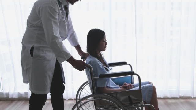 Arzt-ist-Ermutigung-und-Empathie-asiatische-Frauen-Patienten,-behinderte-Bein-sitzen-im-Rollstuhl-in-einem-Haus-oder-Krankenhaus,-das-Sonnenlicht-aus-dem-Fenster-hat.