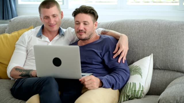 Gay-couple-relaxing-on-couch-using-laptop-computer.-Browsing.
