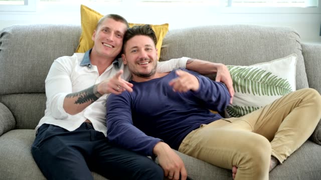 Gay-couple-relaxing-on-couch-watching-tv.-Laughing-together.