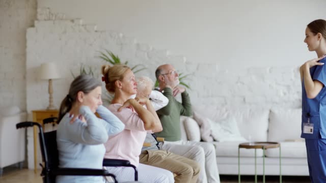 Captura-de-seguimiento-de-vista-lateral-de-la-enfermera-joven-y-grupo-de-pacientes-de-la-tercera-edad,-incluyendo-los-discapacitados-haciendo-ejercicio-de-rotación-de-brazos-juntos-en-el-hogar-de-ancianos