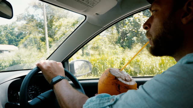 In-car-close-up-shot-of-relaxed-businessman-with-smart-watch-driving-car,-enjoying-exotic-fruit-drink-on-summer-vacation