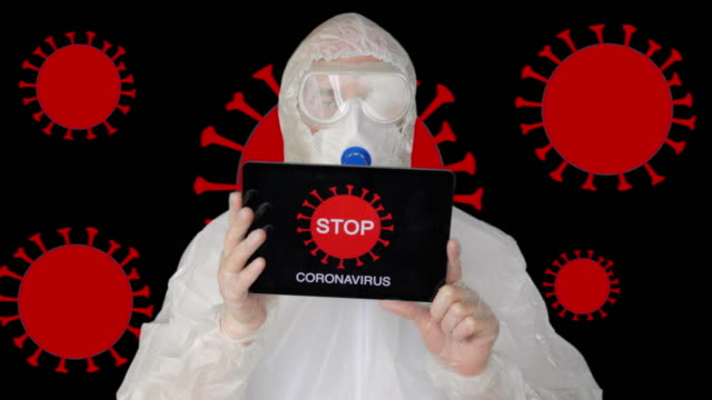 Bio-engineer-in-protective-suit-and-face-mask-showing-tablet-pc-with-sign-stop-corona-virus.-Man-in-protective-coat-and-mask-holding-tablet-with-microbe-molecules.-Covid-19-pandemia.