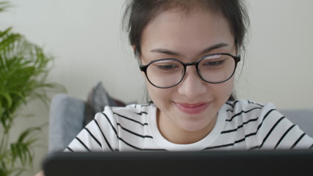 Primer-plano-de-la-mujer-asiática-cara-Gafas-de-desgaste-usando-un-ordenador-portátil-y-sonrisa-feliz,-aprendizaje-en-línea-en-el-concepto-de-casa
