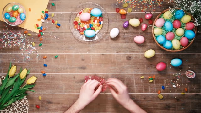 Man-putting-candys-in-the-bag-on-table-decorated-with-easter-eggs.-Top-view