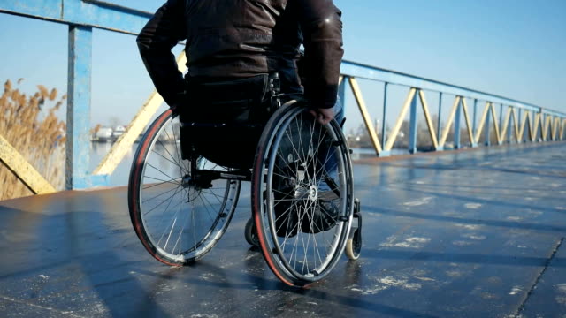 Disabled-man-in-wheelchair-pushing-himself-outdoors-on-bridge