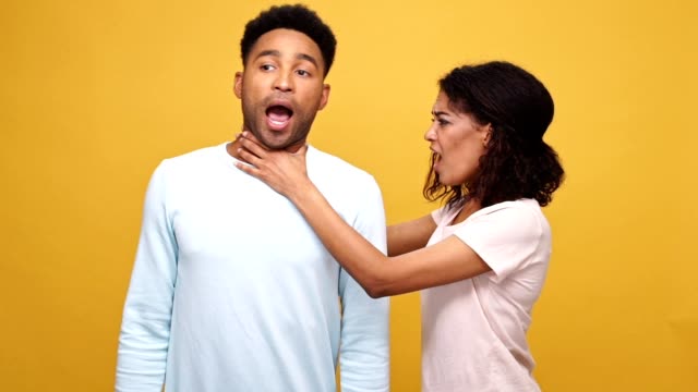 Angry-young-african-woman-strangling-her-boyfriend-isolated-over-yellow-background