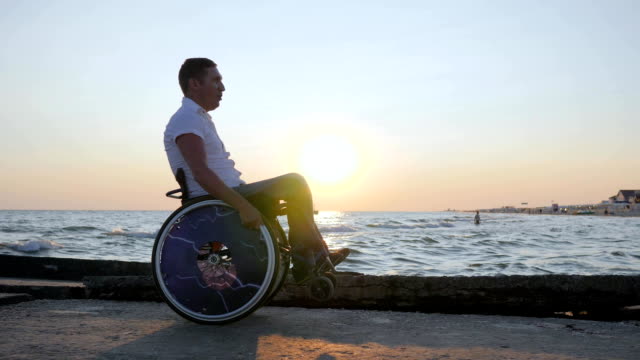 lisiado-hombre-empuja-a-sí-mismo-en-el-mar-de-fondo-puesta-de-sol-y-disfrutar-de-la-naturaleza,-persona-discapacitada-en-silla-de-ruedas