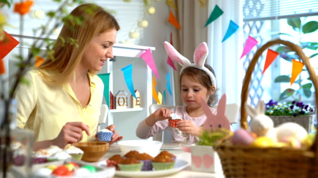 Joven-madre-y-su-pequeña-hija-con-orejas-de-conejo-divertidos-cocinar-cupcakes-de-Pascua