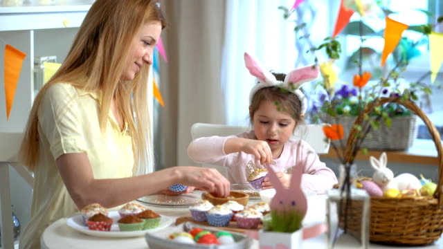 Joven-madre-y-su-pequeña-hija-con-orejas-de-conejo-divertidos-cocinar-cupcakes-de-Pascua