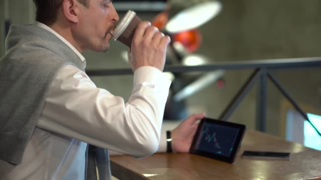 Reife,-gut-aussehender-Mann-trinkt-Kaffee-und-überwacht-Kryptowährung-Handel-auf-Tablet-in-einem-café