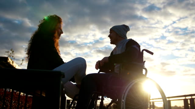 Glückliches-Paar---behinderten-jungen-Mann-im-Rollstuhl-mit-jungen-Frau,-die-zusammen-den-Sonnenuntergang-genießen