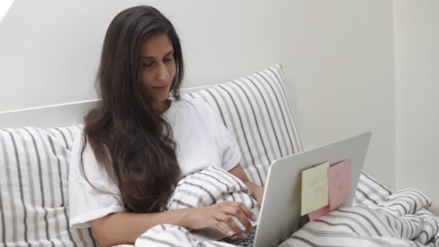 mujer-joven-y-bonita-está-escribiendo-texto-en-laptop-acostado-en-la-cama-en-su-habitación