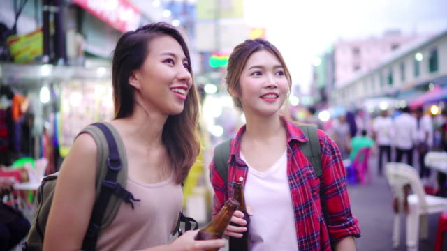 Viajero-mochilero-mujeres-asiáticas-lesbianas-lgbt-par-de-viajes-en-Bangkok,-Tailandia.-Mujer-bebiendo-alcohol-o-cerveza-en-el-Khaosan-Road-la-calle-más-famosa-de-Bangkok.
