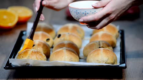Hot-cross-buns-on-baking-tray.-Female-hands-cover-with-syrup.
