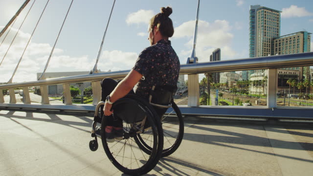 Junge-glücklich-Behinderte-Wheelie-im-Rollstuhl-über-Brücke-in-Stadt-mit-Blendenfleck-zu-tun