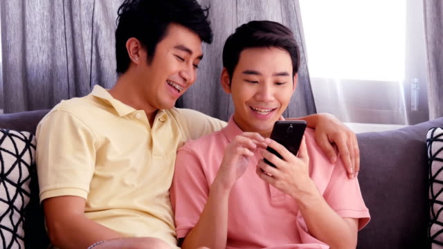 Gay-couple-using-smartphone-together-with-happy-emotion.-People-with-gay,-homosexual,-lifestyle-and-technology-concept.