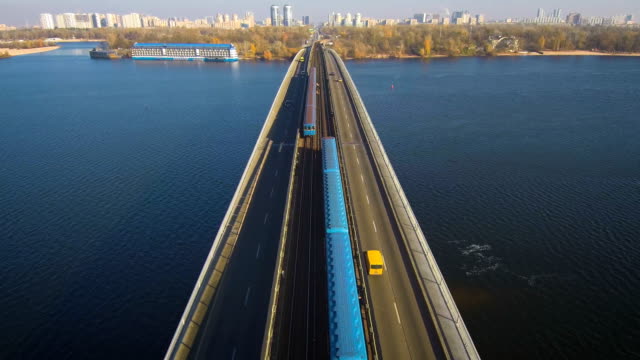 Vista-aérea,-superior-de-Drone:-Metro-tren-viaja-a-través-de-un-puente-con-autos-y-camiones.