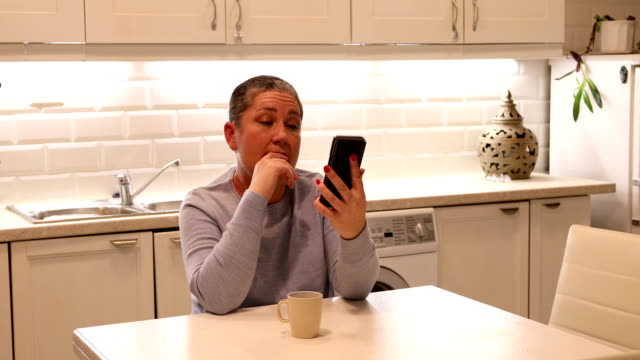 Mujer-con-pelo-corto-gris-usando-smartphone-en-la-cocina
