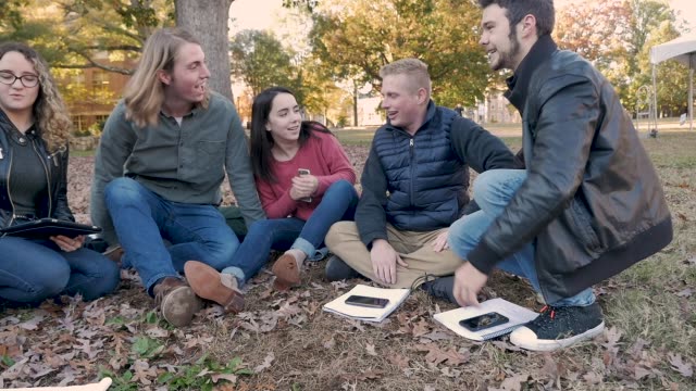 College-Freunde-sitzen-draußen-lachend,-während-sie-digitale-Technologie-halten