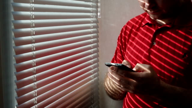 Mann-steht-in-der-Nähe-von-Fenster-im-Hotelzimmer-und-nutzt-Smartphone