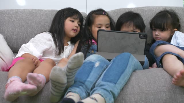 Gruppe-von-Kindern,-die-mit-digitalem-Tablet-zusammen-auf-dem-Sofa-zu-Hause-spielen,-und-lächelnd,-Kinder-auf-digitalem-Tablet-im-Wohnzimmer.