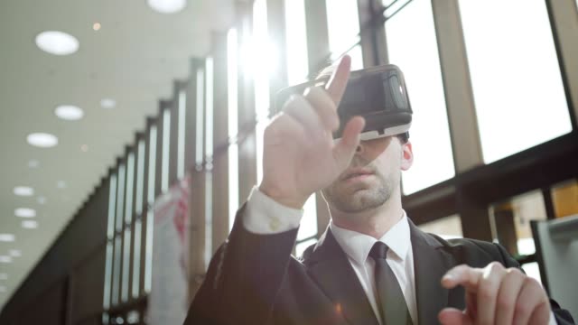 Medium-shot-of-modern-businessman-in-suit-and-tie-wearing-VR-glasses-and-exploring-visualization-in-sunlight