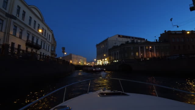 Night-walk-through-the-canals-of-St.-Petersburg,-Russia.-On-the-river-pass-passenger-boats.-The-ship-turns-on-the-water-and-floats-towards-the-bridge