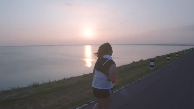 Asian-women-jogging-in-the-street-in-the-early-morning-sunlight-at-water-storage-Pa-Sak-Jolasid-Dam.-concept-of-losing-weight-with-exercise-for-health.-Slow-motion,-Rear-View
