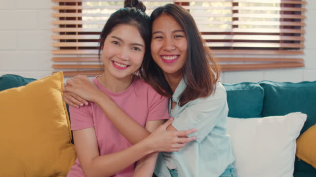 Retrato-Joven-Asiática-Pareja-lesbiana-sintiendo-feliz-sonrisa-dentada-mirando-a-la-cámara-mientras-está-acostado-sofá-en-la-sala-de-estar-en-casa.