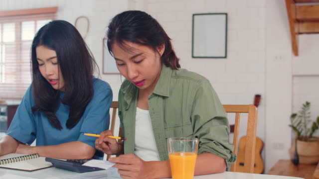 Business-Asian-Lesben-Paar-mit-Taschenrechner-Rekord-Budget,-Steuer,-Finanzdokument-auf-Laptop-in-der-Küche-arbeiten.