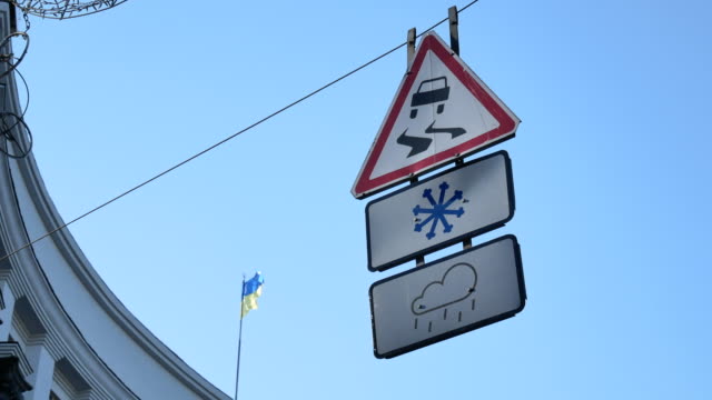 Road-signs-waving-on-a-wire-under-the-street---slippery-road-when-it-is-snowy-or-rainy-weather