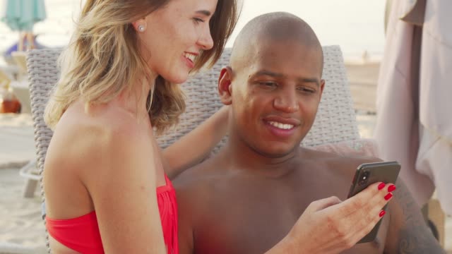 Charming-multiethnic-couple-laughing-watching-something-funny-on-smart-phone