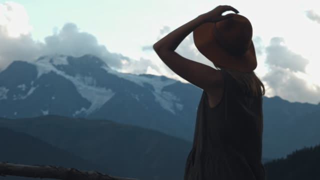 Back-view-of-hipster-girl-in-hat-excited-with-journey-to-mountains,-happy-young-woman-wanderlust-looking-alps-peaks-feeling-freedom-and-happiness-close-to-nature.
