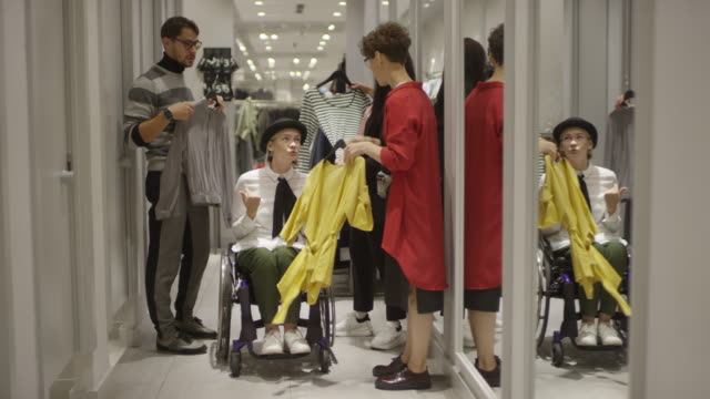 Freunde-helfen-Frau-im-Rollstuhl-Einkaufen-für-Kleidung