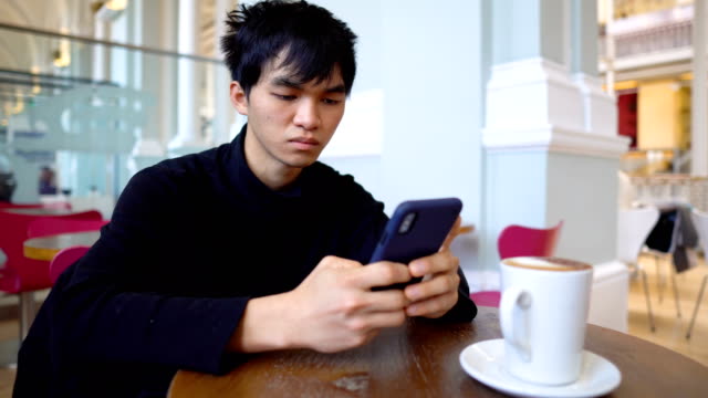 Junge-asiatische-Mann-SMS-am-Telefon-während-sitzen-im-Cafe