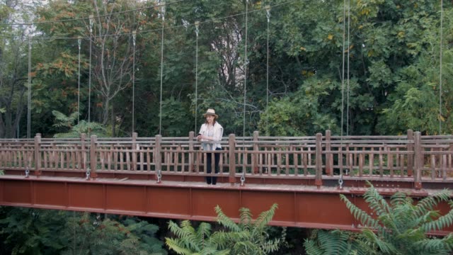 Millennial-Hipster-Touristin-mit-Smartphone-auf-der-Brücke-im-Dschungel