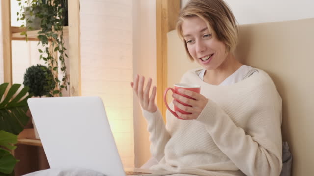 Glückliche-Frau-Video-chatten-mit-Laptop-im-Bett