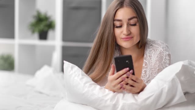 Porträt-schöne-Frau-in-Pyjamas-mit-Smartphone-auf-dem-Bett-liegen.-Nahaufnahme-auf-4k-RED-Kamera