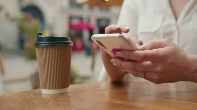Close-up-shooting.-The-girl-is-texting-on-her-smartphone.-There-is-a-cup-of-coffee-on-the-table.-She-is-sitting-in-a-cafe.-4K