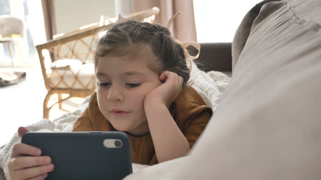 Little-girl-watches-cartoons-on-smartphone-on-soft-sofa