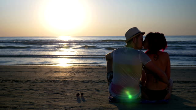 Couple-kissing-on-sandy-beach-at-beautiful-sunrise