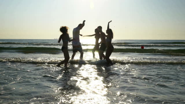 Gruppe-von-Freunden-in-Richtung-Meer-laufen-und-tanzen-mit-den-Füßen-im-Wasser