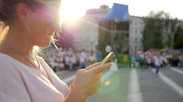 happy-female-holds-android-standing-in-downtown,-women-sitting-on-mobile-Internet-Outdoors,-young-woman