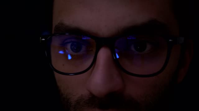 Portrait-Man-earns-bitcoins-on-his-bitcoin-farm.-Closeup-shot-of-boy-in-glasses-surfing-internet-at-night.-Close-up-of-young-man-reading-his-tablet-in-the-dark.-Black-background-in-focus.-Slow-Motion