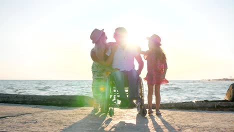 Joyful-Family-On-background-sea,-man-in-wheelchair-with-little-Girl-and-pregnant-woman-outdoors,-invalid-with-wife